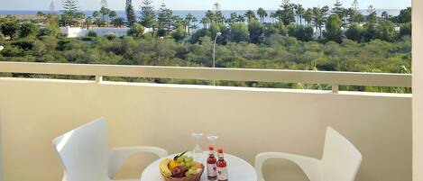 A balcony with two white chairs, a small round table, a fruit basket, and two bottles of red wine.