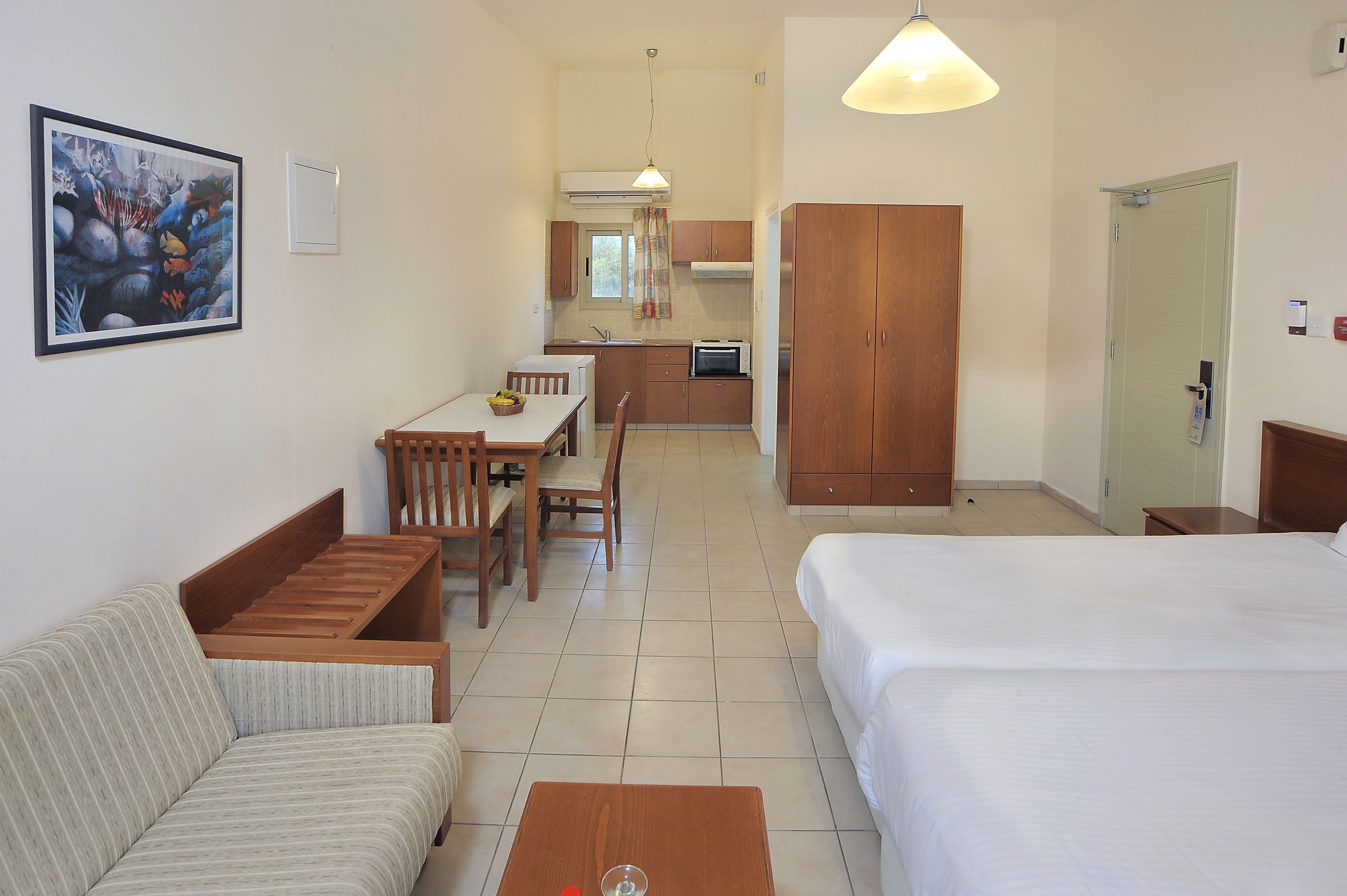 Habitación de hotel con cama, sofá, mesa de comedor con sillas, zona de cocina y armario de madera.