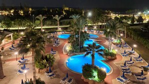 Ein Poolbereich eines Resorts mit mehreren Pools, Liegestühlen und Palmen.