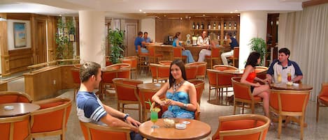 Um saguão de hotel com várias áreas de estar, um bar e uma mesa de recepção.