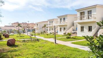 Una hilera de edificios modernos de dos pisos con balcones, rodeada de céspedes cuidados y pequeños árboles.