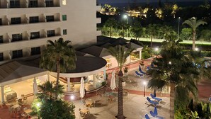 Ein Hotelinnenhof mit Außenbestuhlung, Palmen und Blick auf das Meer bei Nacht.