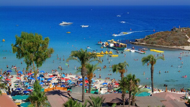 Ein Strand mit vielen Sonnenschirmen und Menschen, die das Wasser genießen.