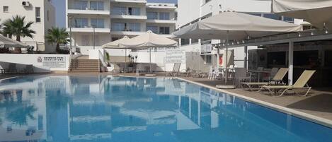 A swimming pool with lounge chairs and umbrellas, surrounded by modern buildings with balconies.