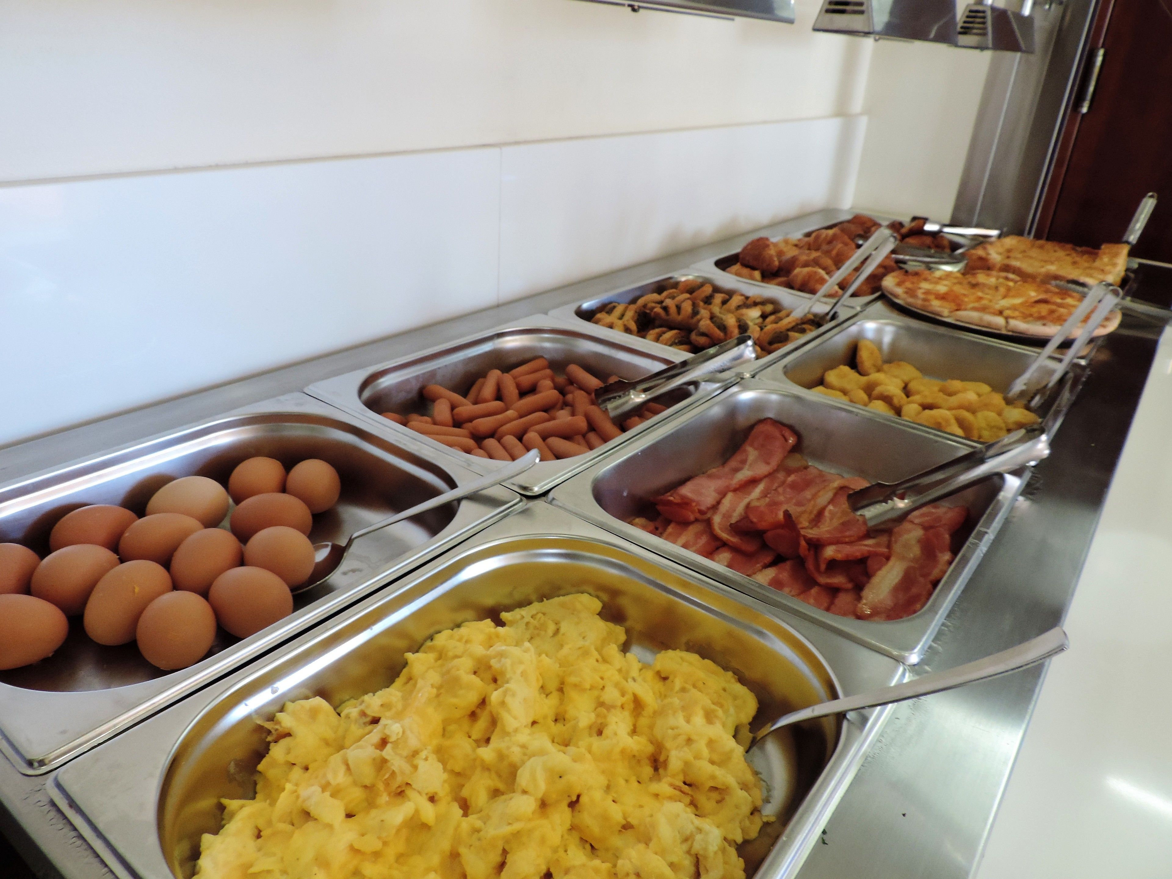 A buffet with various food options including eggs, bacon, sausages, and scrambled eggs.