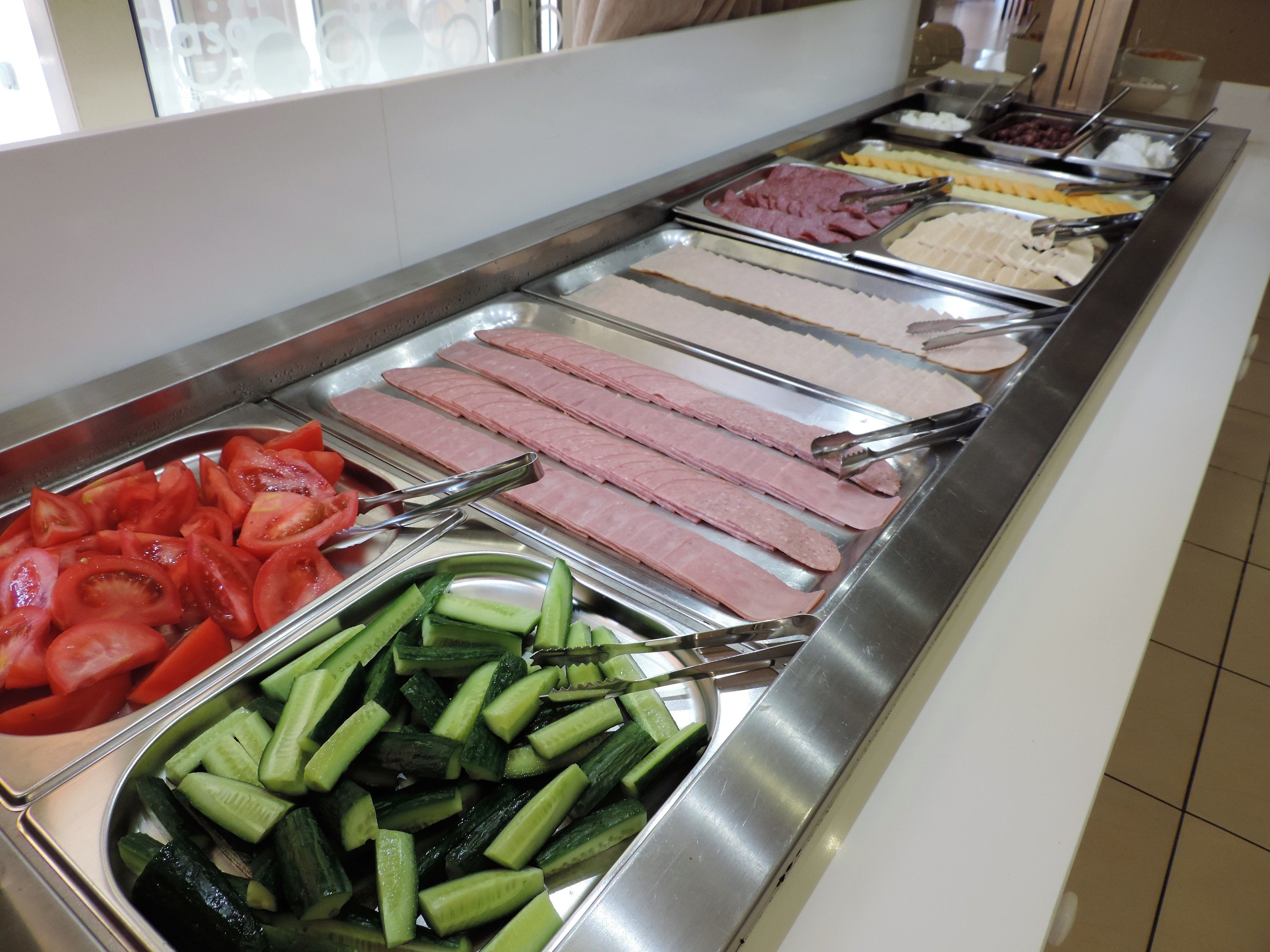 A buffet with various food options including sliced tomatoes, cucumbers, and different types of meat.