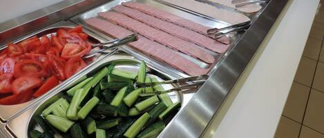 A buffet with various food options including sliced tomatoes, cucumbers, and different types of meat.