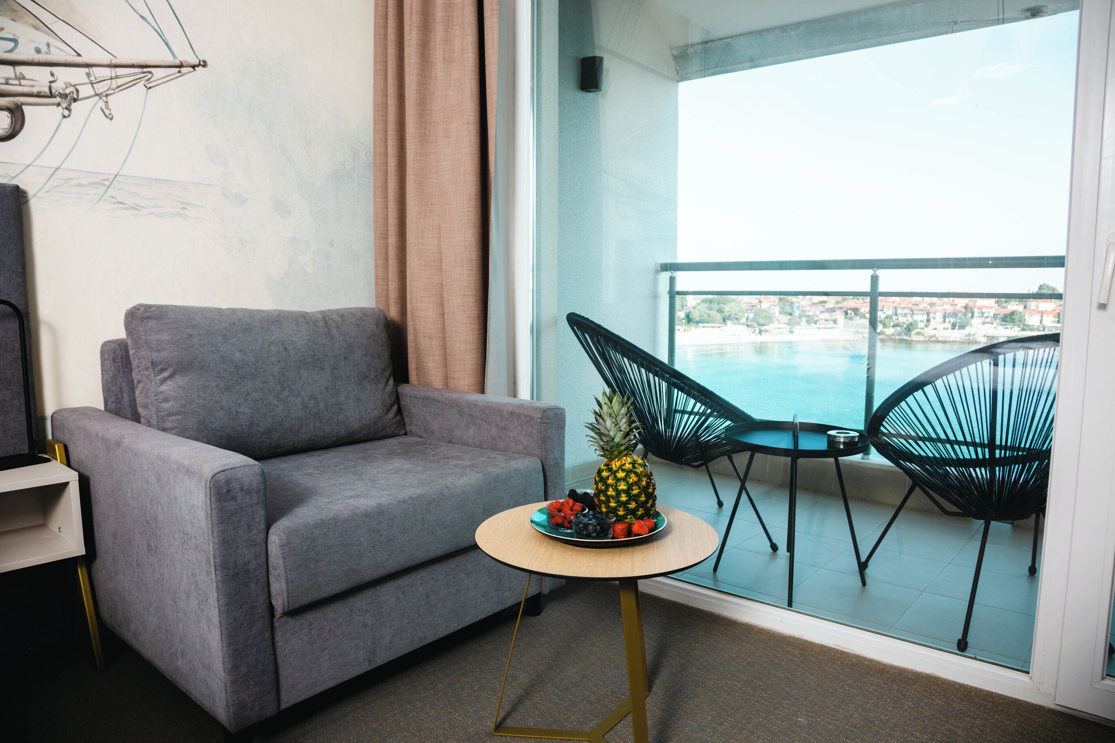 A balcony with a grey sofa, a small round table with fruit, and two black chairs.