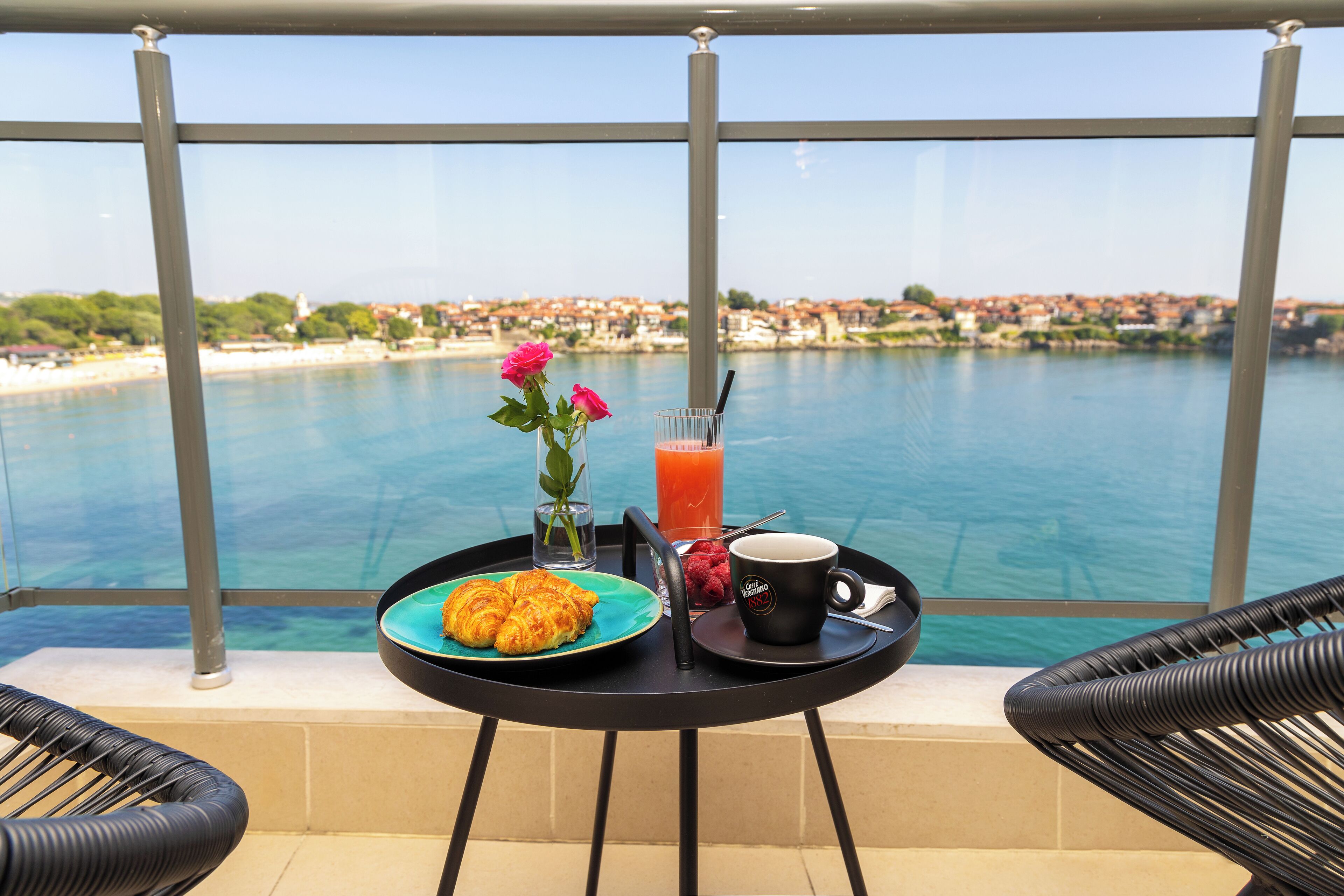 A balcony with a table set for breakfast, overlooking a body of water and a distant town.