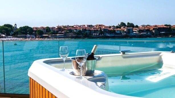 Un jacuzzi con dos vasos y una botella, con vista a un pueblo costero.