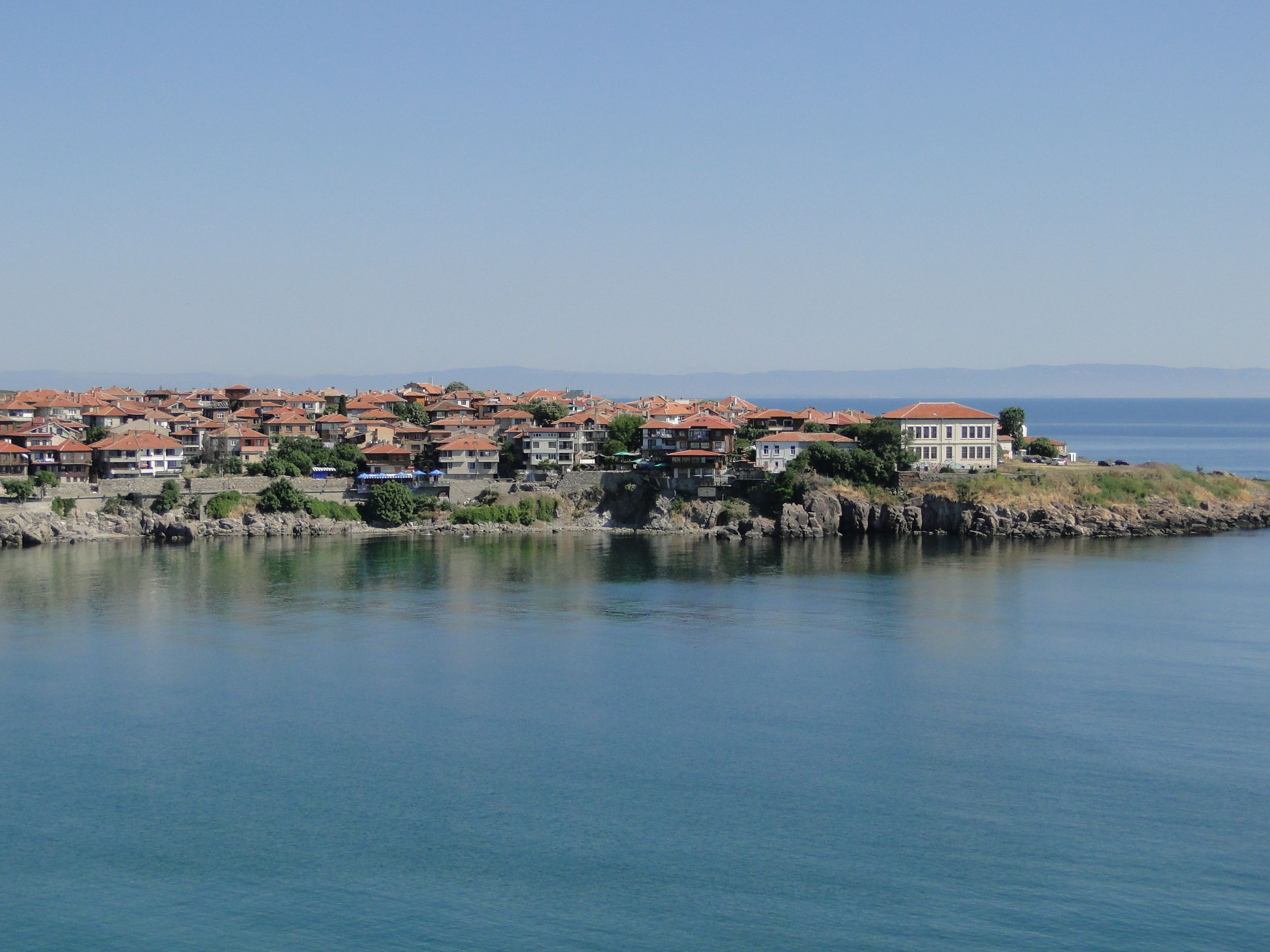 Un pueblo costero con edificios a lo largo de la orilla, cielo despejado y agua tranquila.