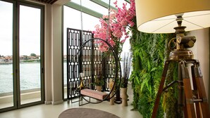 Una habitación con vista a un cuerpo de agua, un sillón colgante, una lámpara y una pared decorada con plantas.