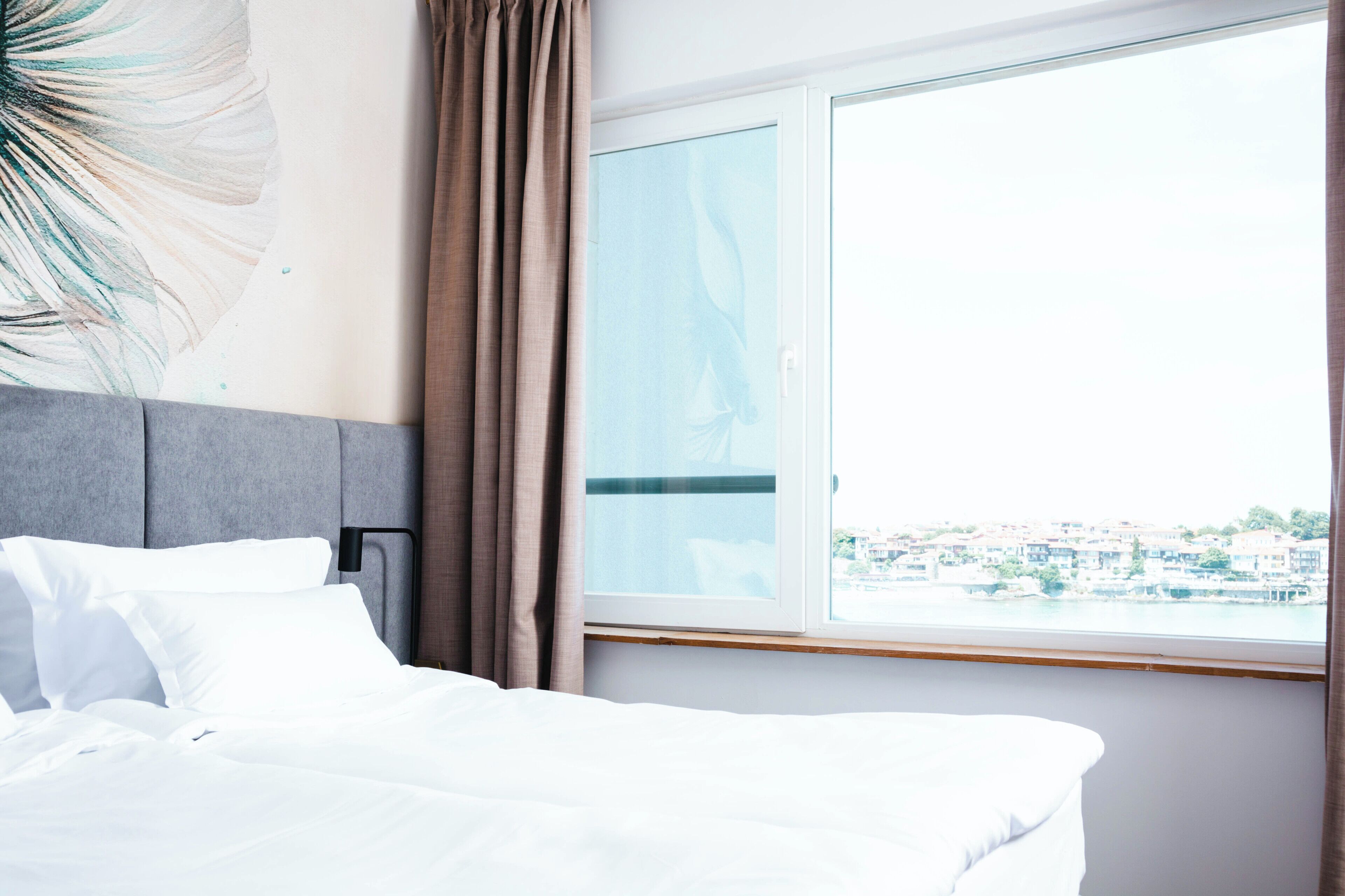Una habitación de hotel con cama, ventana y cortina, y vista a edificios.