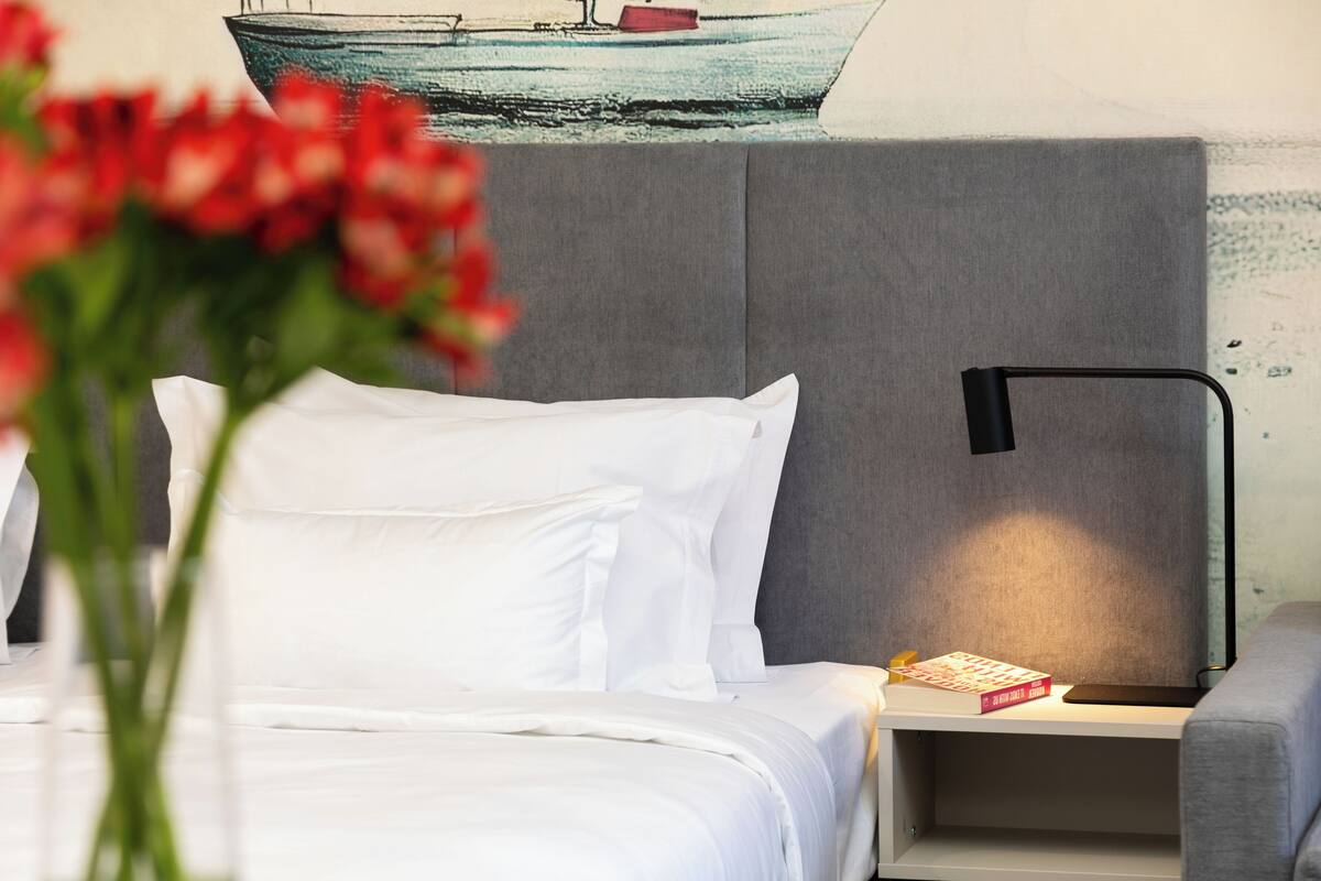 A hotel room with a bed, a nightstand, a lamp, and a book.