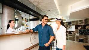 Zona de recepción de un hotel con diseño moderno, que incluye un mostrador de recepción, un área de bar con estantes llenos de botellas y una pared decorativa con patrones geométricos.