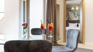 Una habitación de hotel con una mesa de vidrio, dos bebidas, una silla y una cama con un cuadro.