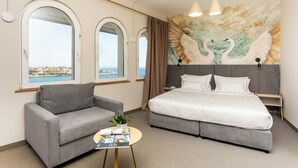 Una habitación de hotel con una cama, un sofá, una mesita con una planta y un mural de cisnes en la pared.