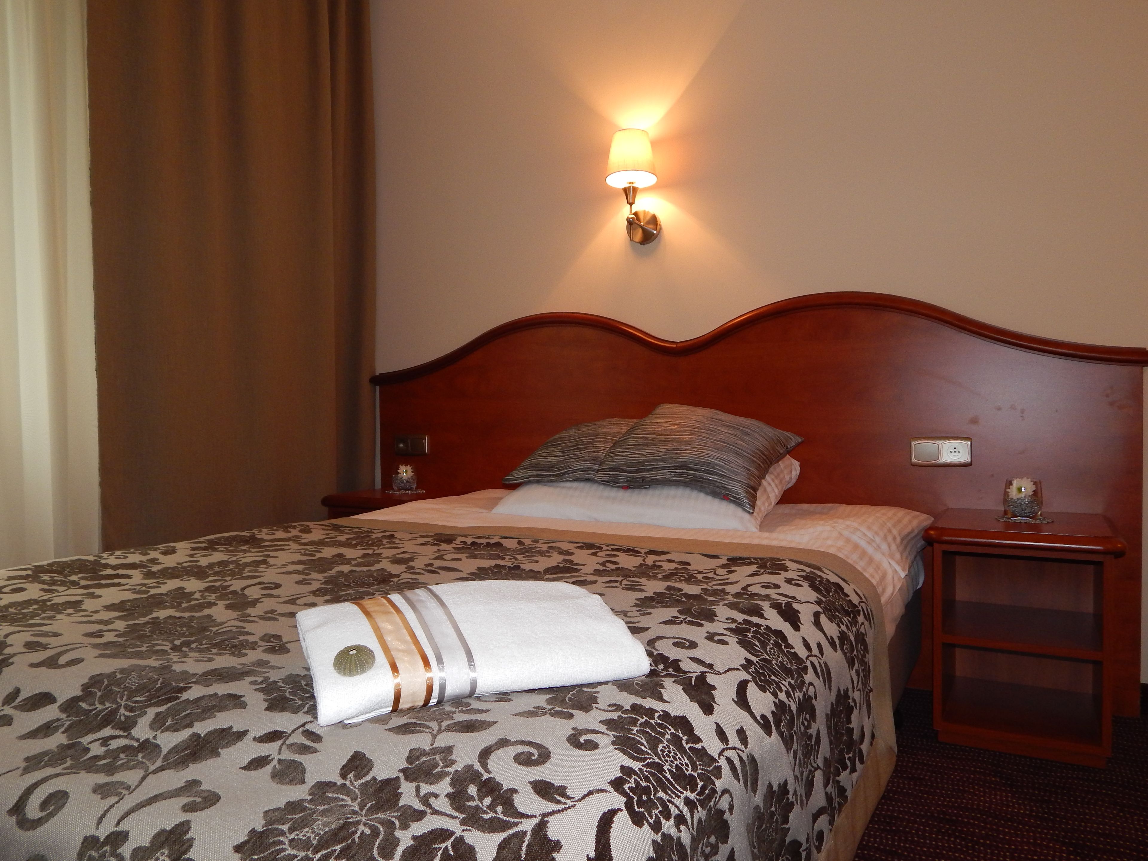 A neatly made bed with a floral-patterned bedspread and a folded towel.