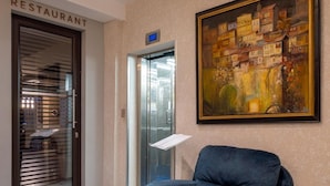 Eine Hotelhalle mit einem Sessel, einem Gemälde, einem Aufzug und einem Schild für das Restaurant.