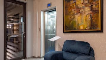 A hotel lobby with a chair, a painting, an elevator, and a restaurant sign.