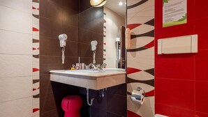 Ein modernes Badezimmer mit Waschbecken, zwei Haartrocknern, einer roten Toilette und einem Mülleimer.