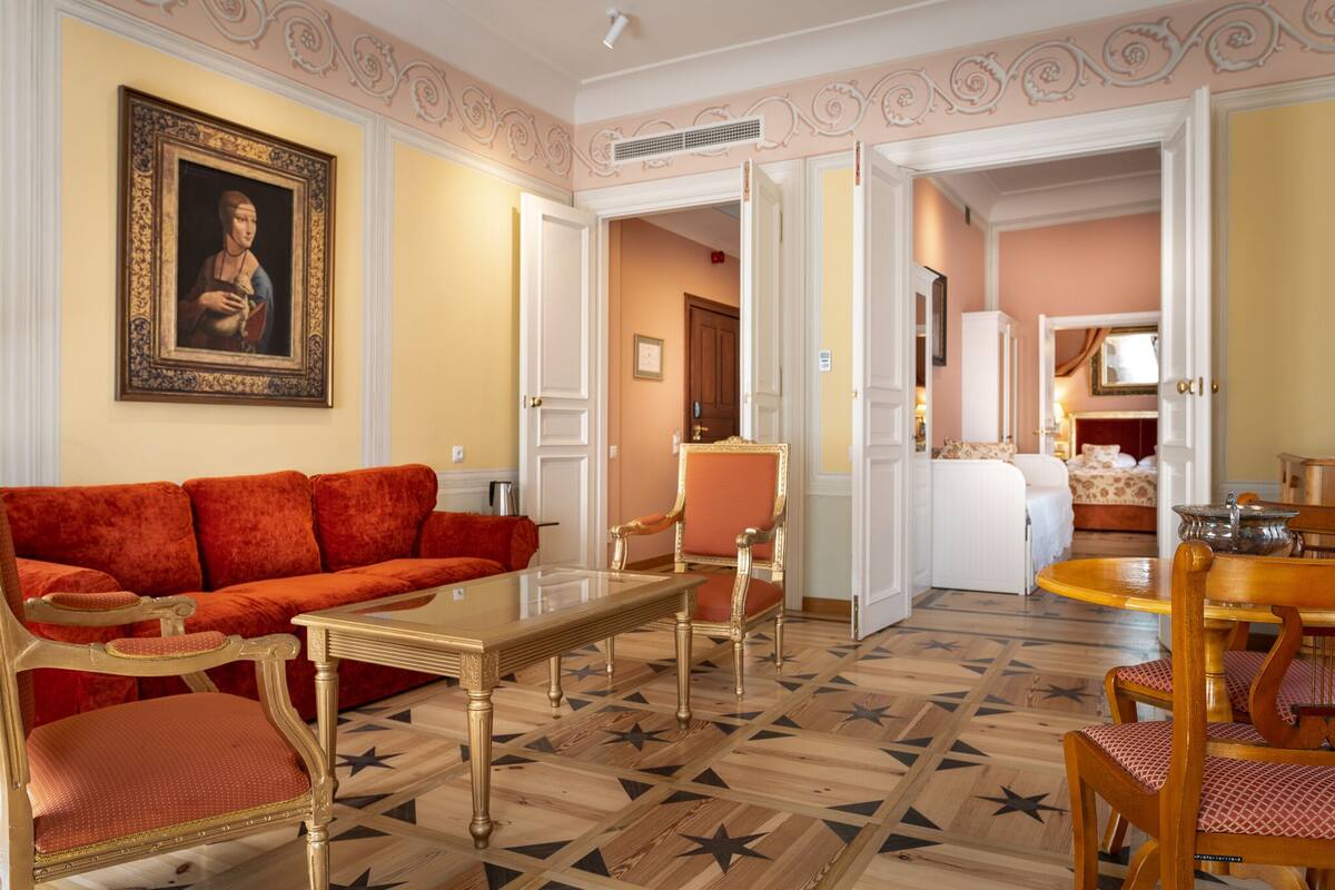 A room with a red sofa, a wooden table, and a chair. There is a painting on the wall and a door leading to another room.