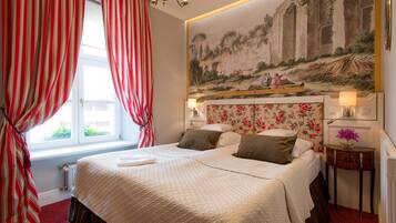 A hotel room with a large bed, red curtains, a floral headboard, and a mural on the wall.