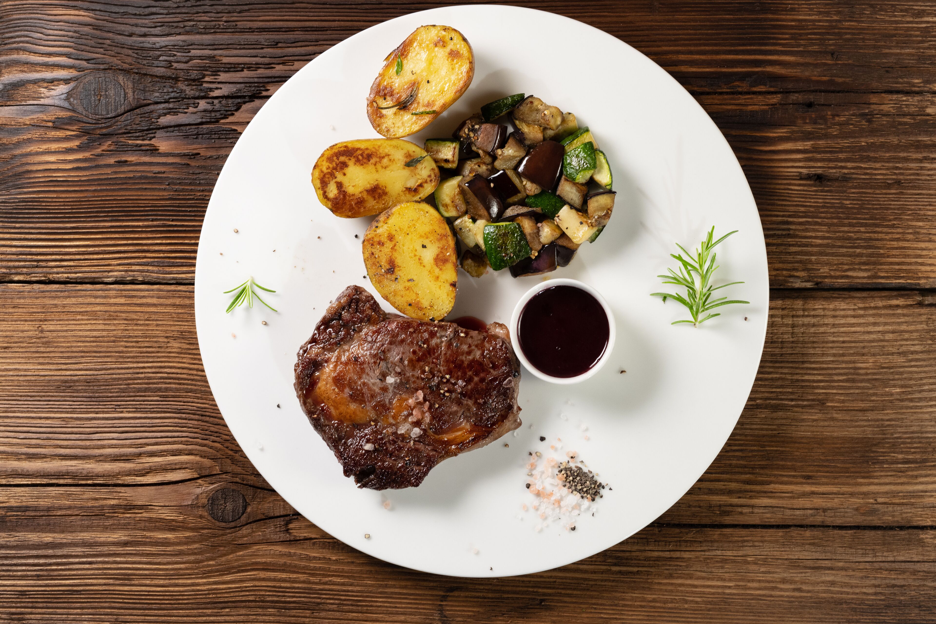 A plate with a steak, roasted potatoes, and a vegetable medley, served on a wooden table.