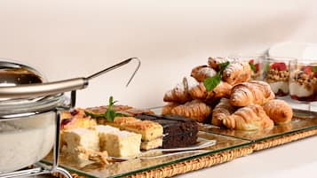 Uma bandeja com diversos doces e sobremesas, incluindo croissants e uma fatia de bolo.