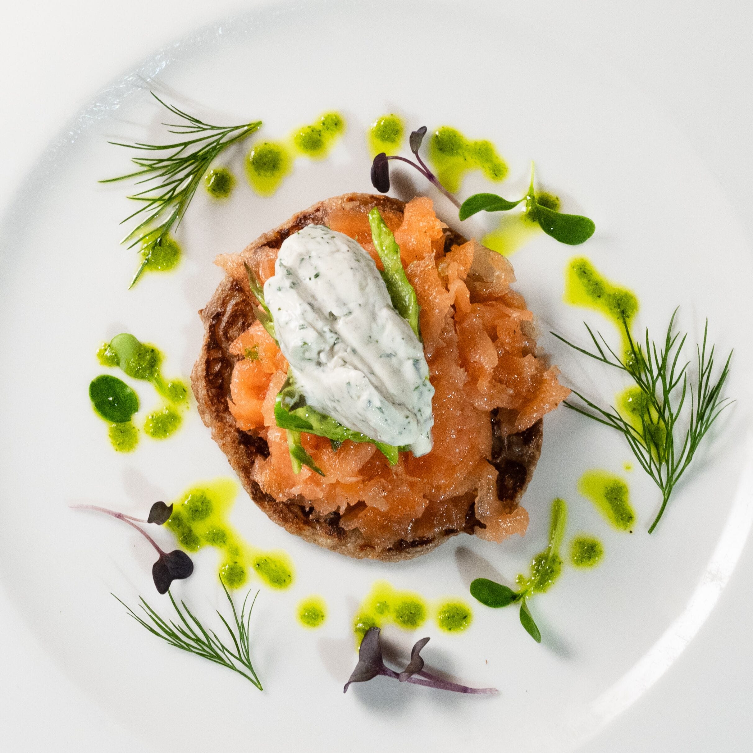 Un plato con una rebanada de pan cubierta de salmón ahumado y una cucharada de crema.