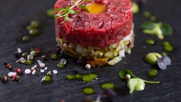 A dish of raw steak tartare with a garnish, surrounded by various condiments and garnishes on a dark slate plate.