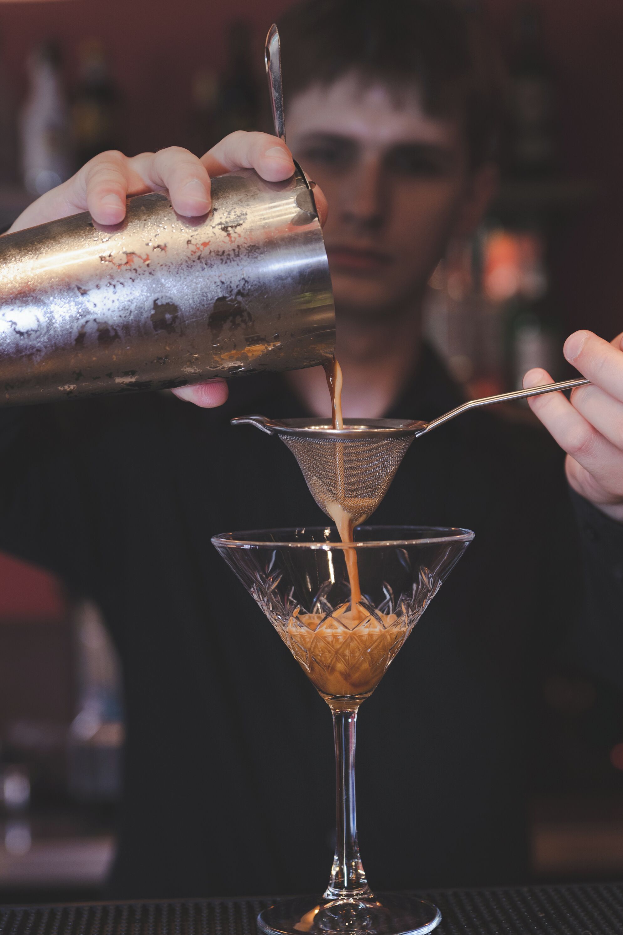 Una persona abocant un líquid d'un xarrup a una copa de martini.