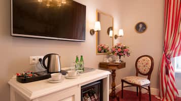 A hotel room with a flat-screen TV, a coffee station, a floral arrangement, and a vintage chair.
