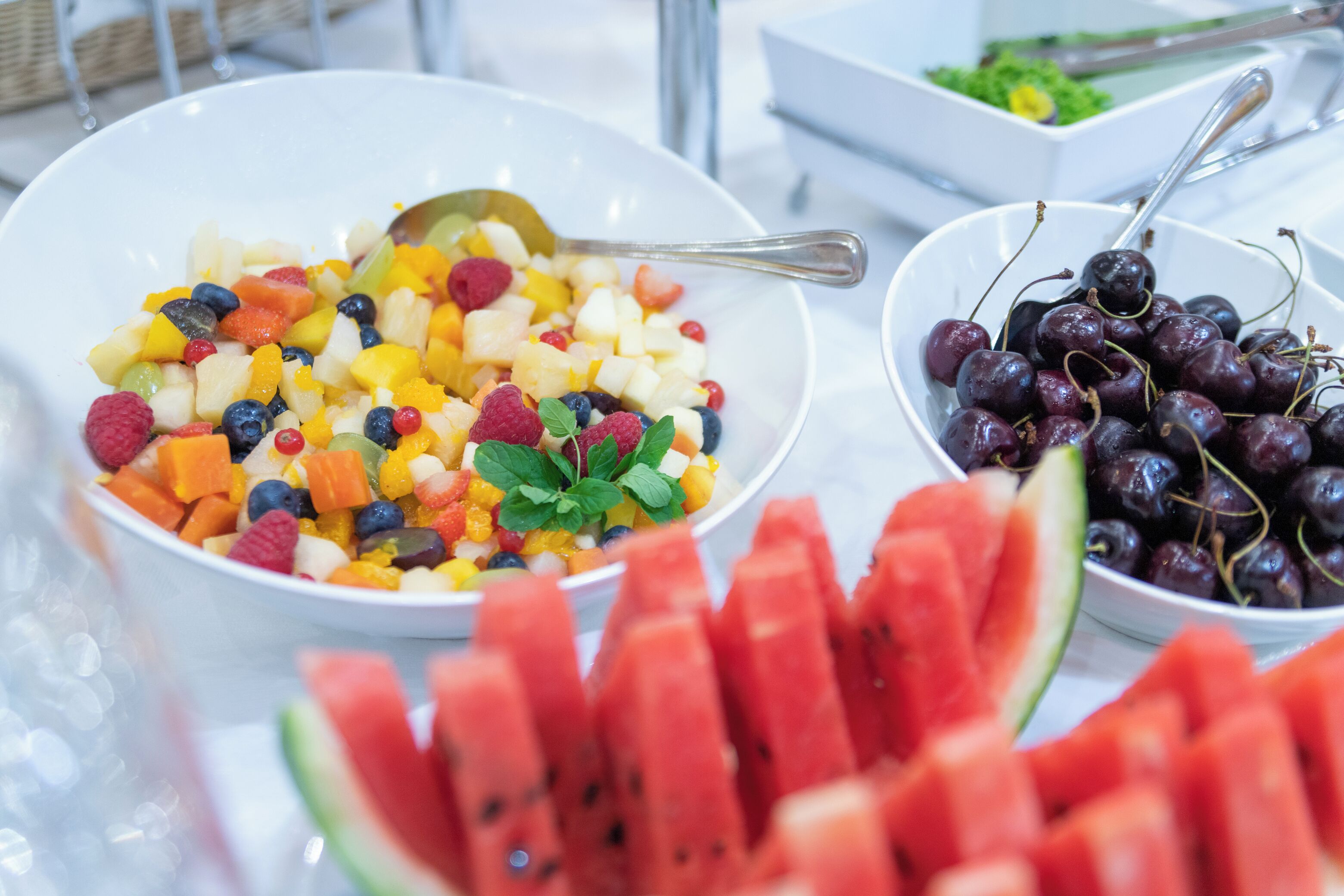 A buffet table with bowls of fruit salad and cherries.