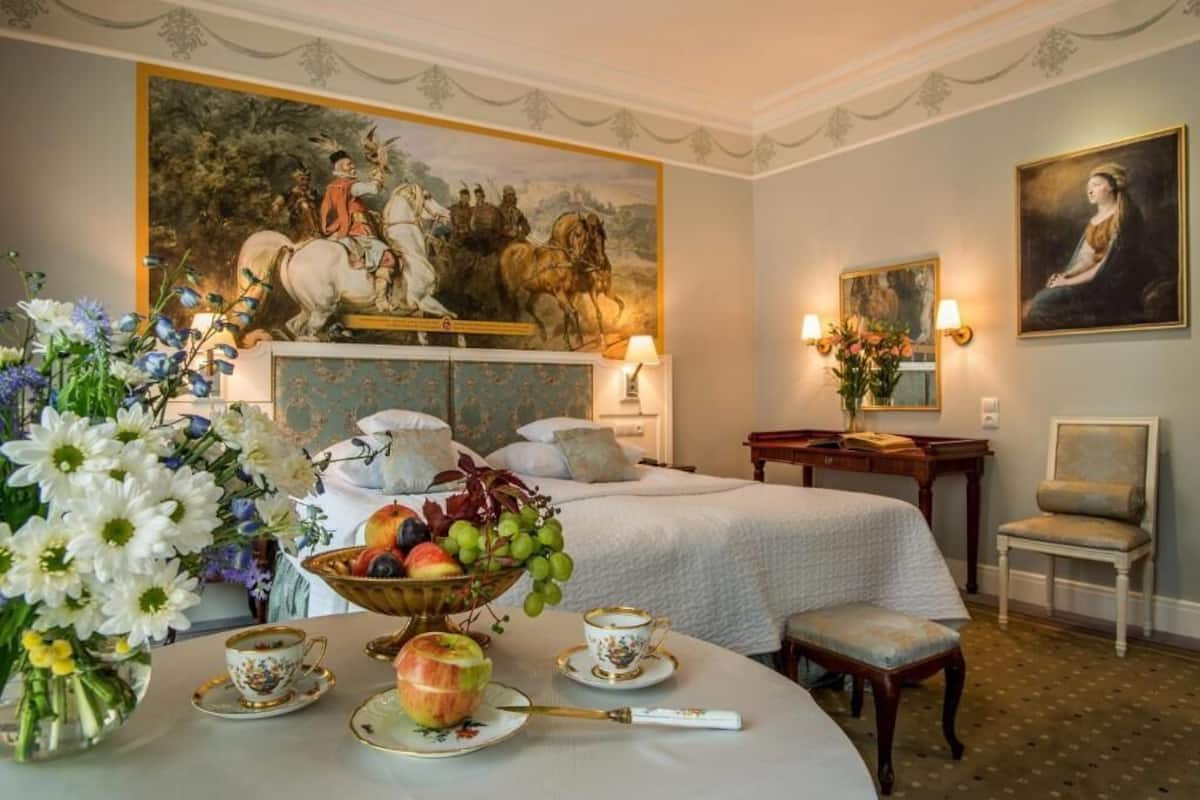Et hotelværelse med en seng, et skrivebord, en stol, et billede og en skål med frugt.