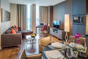 Una habitación de hotel moderna con sofá, mesa de comedor, escritorio con computadora portátil, televisor y microondas.