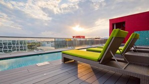 Zona de piscina en la azotea con sillones de descanso y una vista despejada del horizonte de la ciudad.