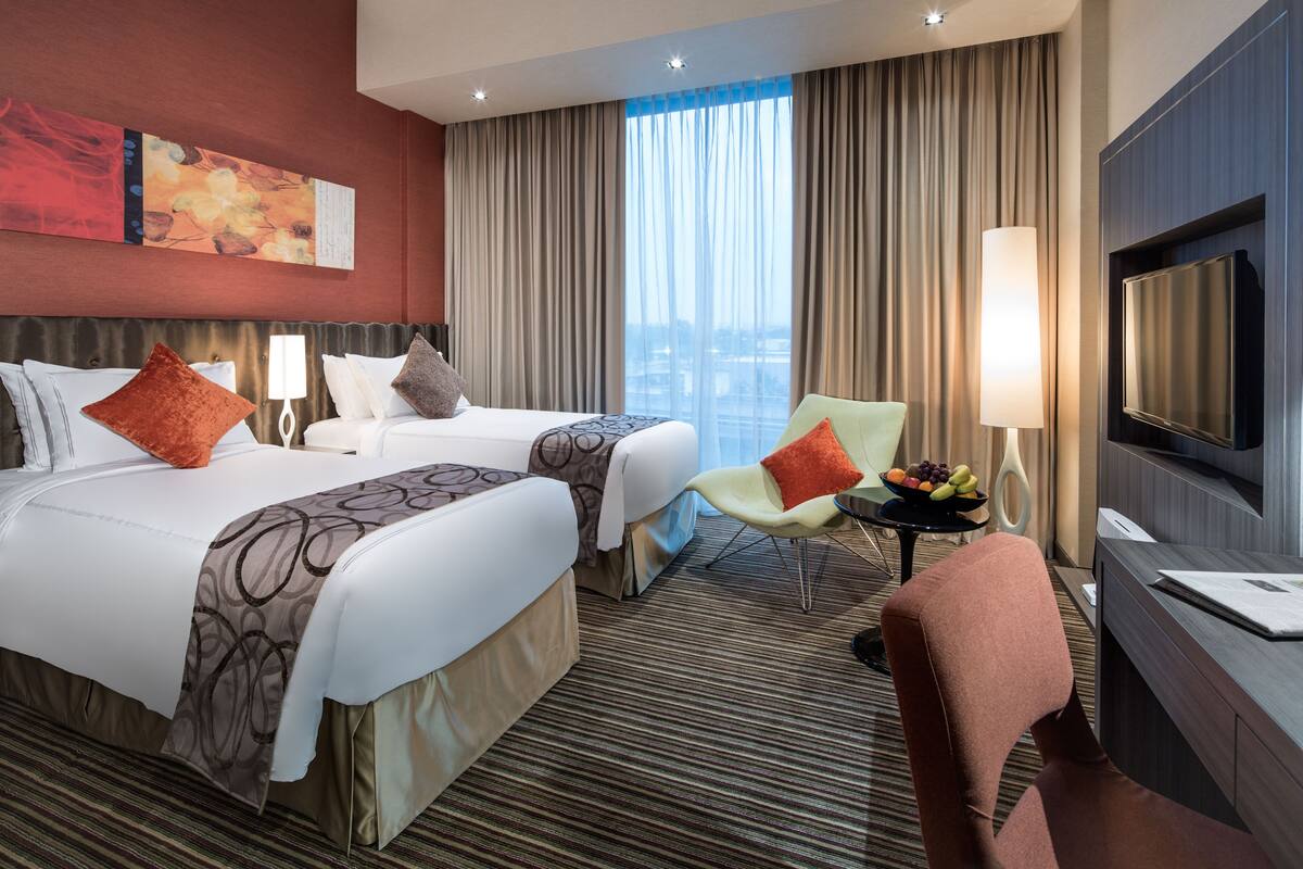 A hotel room with two beds, a TV, a desk, and a chair.
