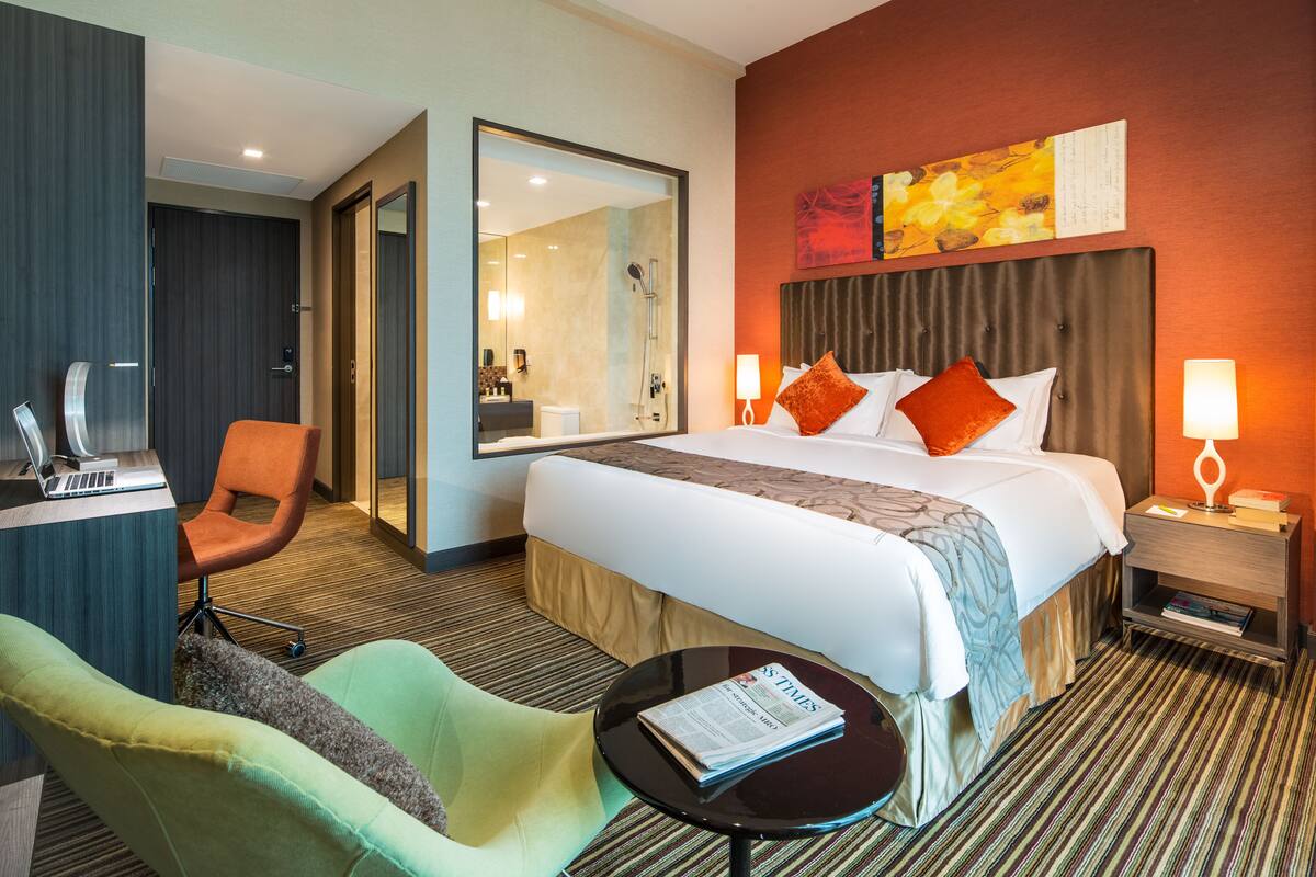 A hotel room with a bed, a desk, a chair, a small table, and a mirror.