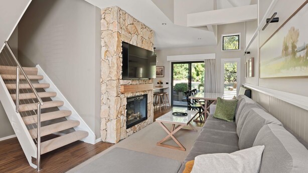 Una sala de estar moderna con chimenea de piedra, una escalera, un sofá y un comedor.