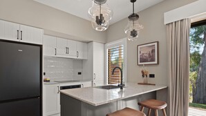 Una cocina moderna con armarios blancos, un refrigerador negro, encimera de granito, dos taburetes de madera e iluminación colgante.