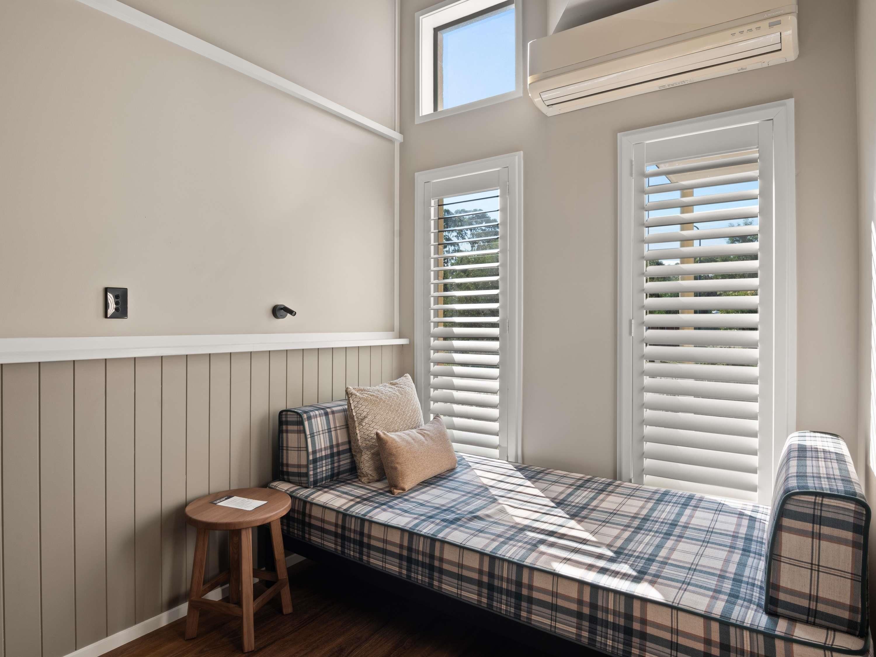 A cozy reading nook with a plaid sofa, a small wooden stool, and a window with blinds.