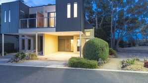 Una casa moderna de dos pisos con balcón, garaje y un jardín delantero cuidado.