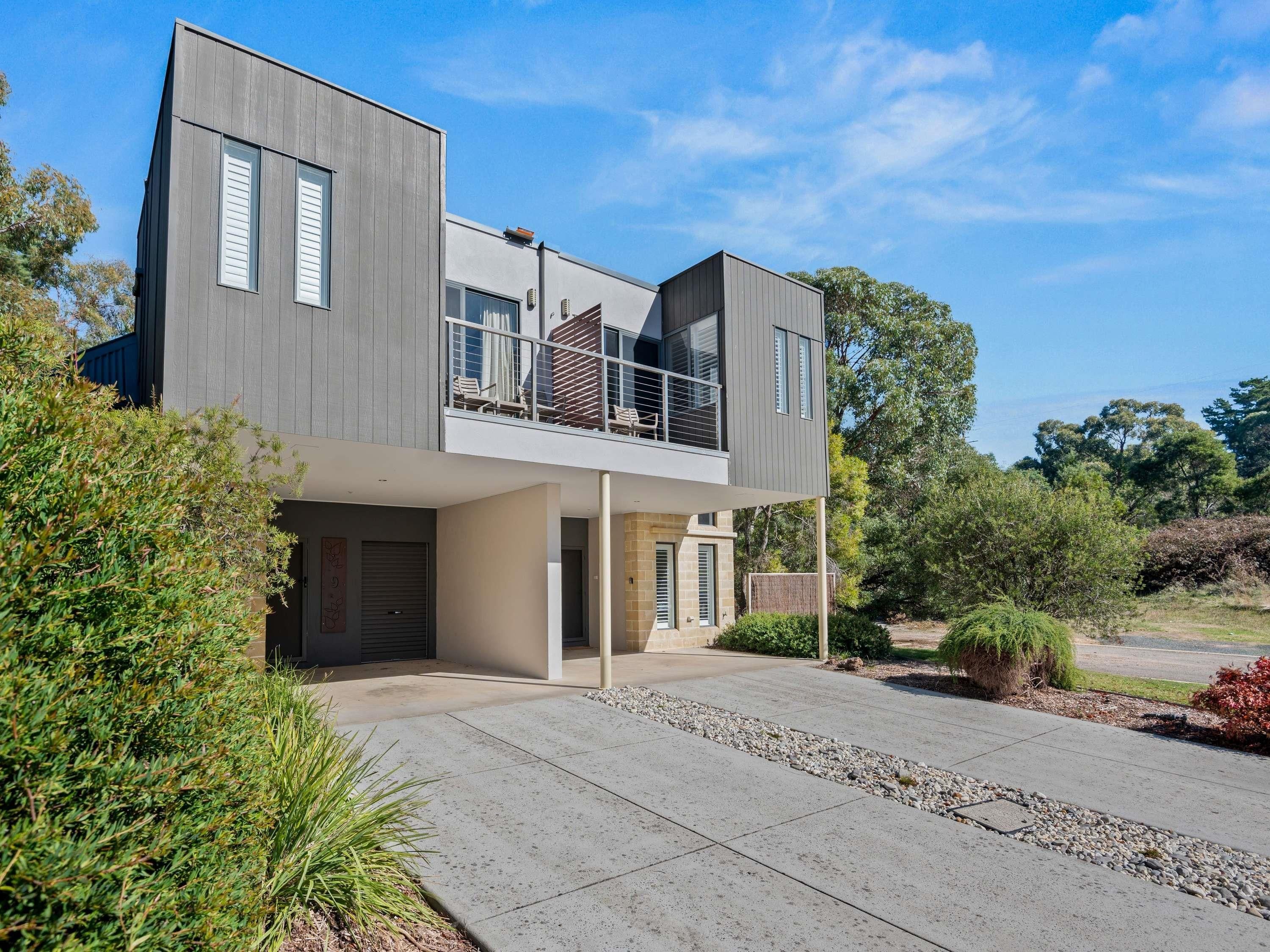 A modern two-story house with a balcony, large windows, and a driveway.