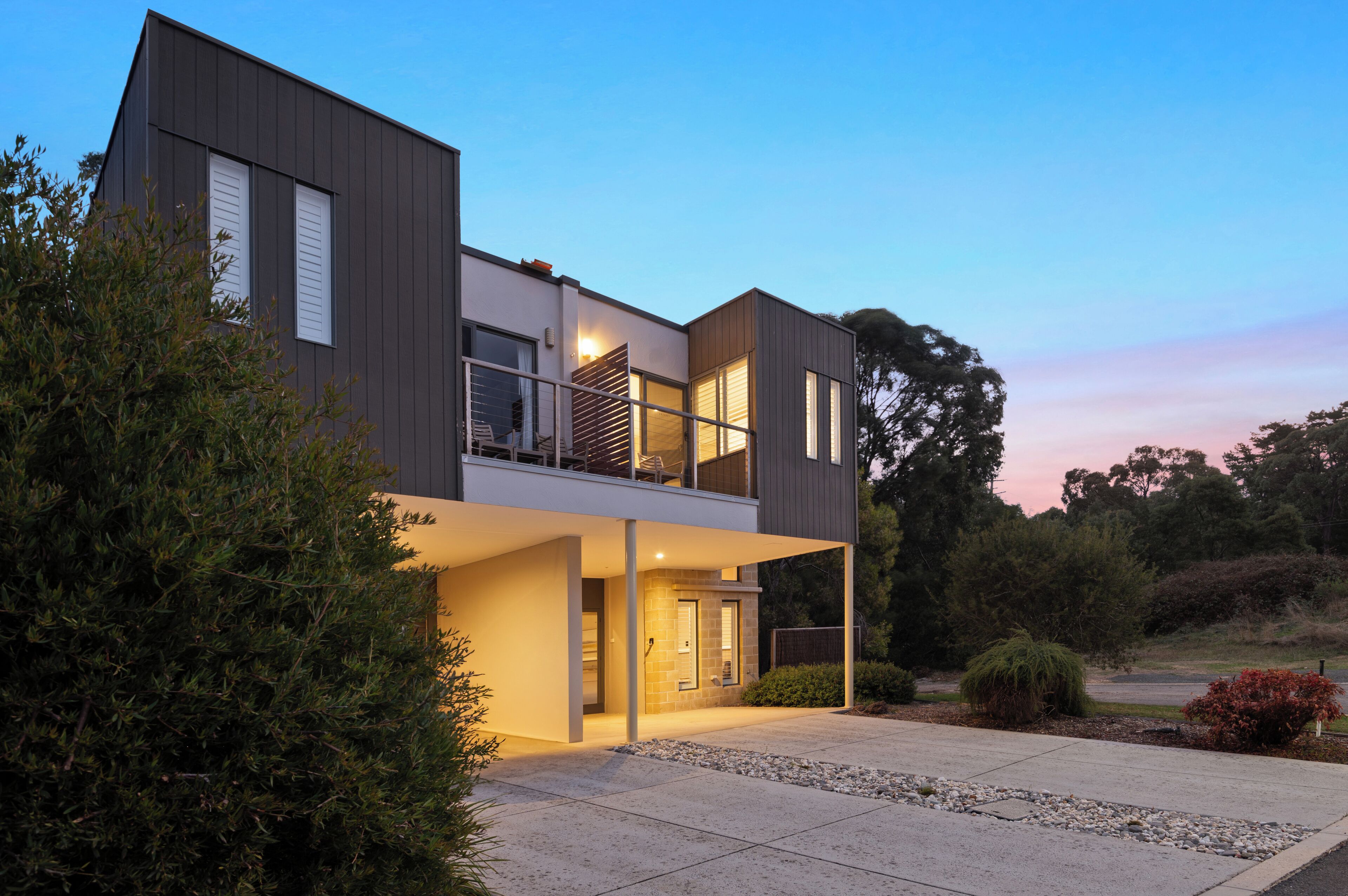 Une maison moderne à deux étages, dotée d’un balcon, de grandes fenêtres et d’une entrée bien éclairée.