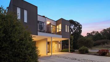 Une maison moderne à deux étages, dotée d’un balcon, de grandes fenêtres et d’une entrée bien éclairée.
