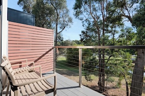 Un banco de madera en un balcón con vistas a árboles y una valla.