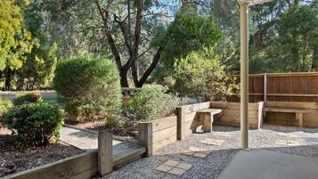A covered outdoor seating area with wooden benches and a pergola, surrounded by gravel and small plants.