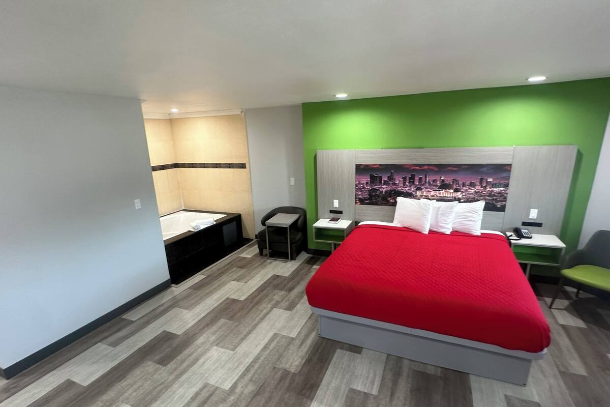 Quarto de hotel com uma cama grande, uma secretária pequena, uma cadeira, uma mesa de cabeceira, banheiro com banheira e um mural de paisagem urbana.