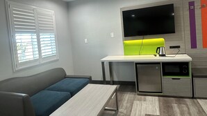 A modern living room with a gray sofa, a small table, a bright green accent wall, a flat-screen TV, and a kitchenette area. - Garden Inn Hotel 花園酒店 - Pasadena, San Gabriel - Los Angeles (Temple City)
